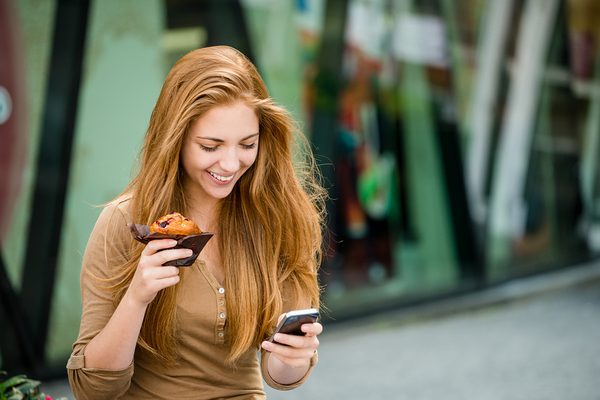 Woman holding a muffin in one hand and a mobile phone in the other.